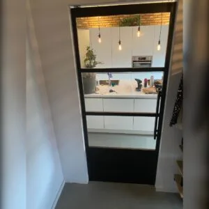 stalen deur met dichte onderplaat en glas met zicht op de keuken